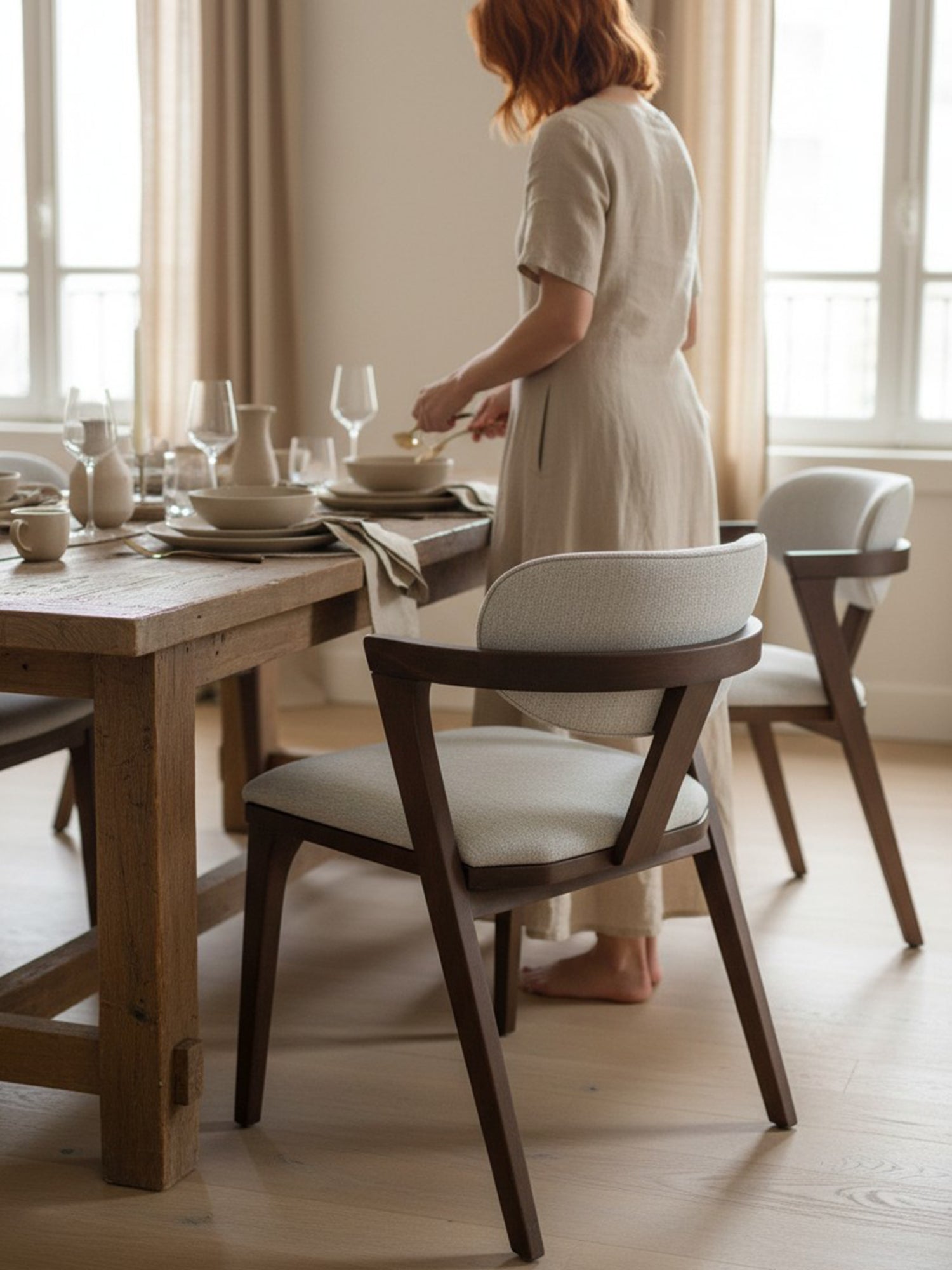 Bobin kollu ahşap sandalye, açık gri döşemeli oturma ve sırt yapısıyla koyu ahşap ayaklar üzerinde ev ortamında yemek masası yanında konumlandırılmış görünüm.
