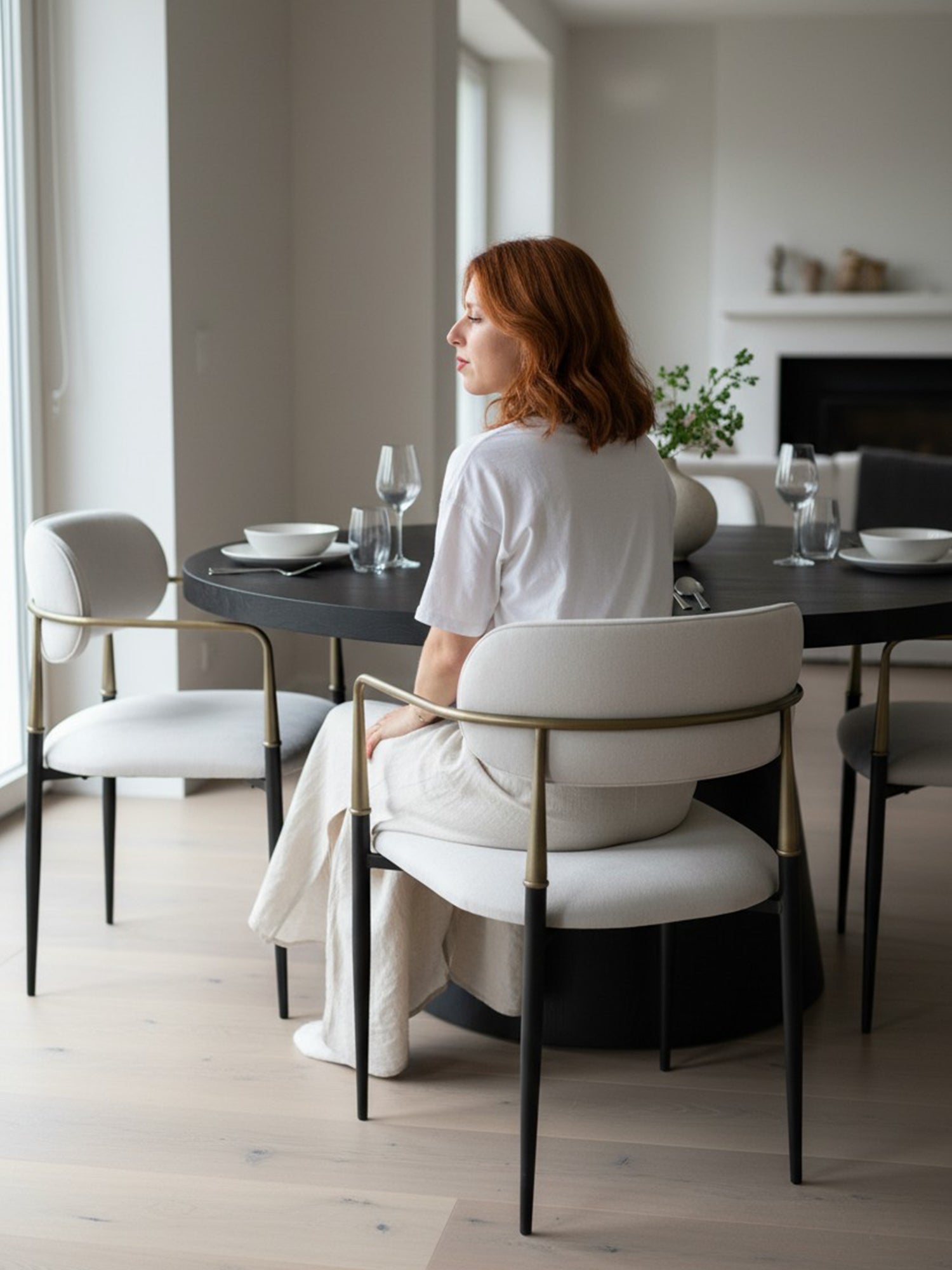 Elegance metal sandalye, açık renk döşemeli oturma ve sırt yapısıyla siyah metal ayaklar ve pirinç renginde kollu tasarımıyla modern bir yemek masasının yanında ev içi kullanımda görünüm.
